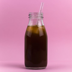 cold drink with ice cubes and cocktail straw in a glass bottle pink background