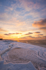 Fototapeta na wymiar a beach under snow and a cold, ice-covered sea during sunset