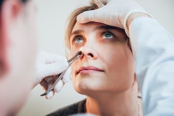 Otolaryngologist examines woman's nose with nasal dilator.