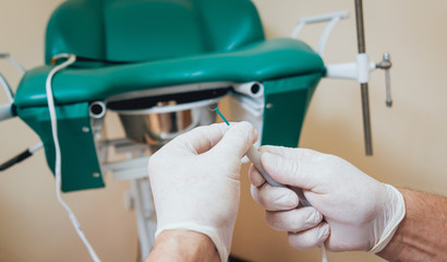 Proctologist holding an anoscope against a proctological chair.