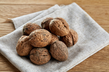 A stack of hard shells of walnuts piled together on light grey fabric cotton tablecloth, selective focus