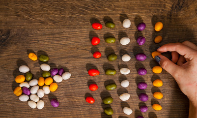 woman's hand collects even row of colorful candies on a wooden background. top view with copy space