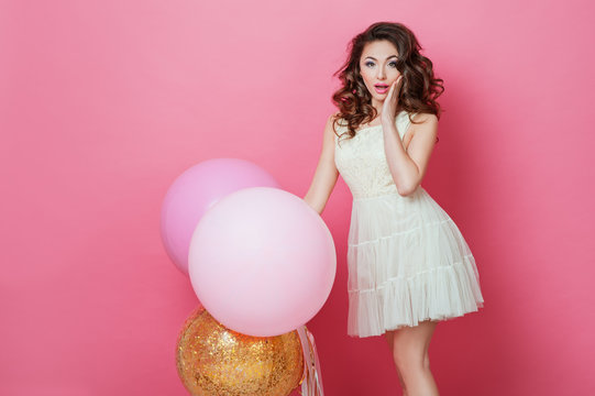 Cheerful Beautiful young girl in dress with sparkle and pink helium balloons enjoying birthday photoshoot dancing and smiling on pink background Surprised woman posing in studio. Fashion Lifestyle