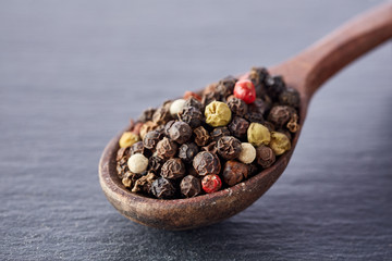 Top view on peppercorn in wooden spoon on dark background, close-up, selective focus