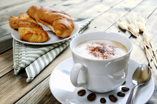 Traditional Italian breakfast with cappuccino and croissants on a rustic wooden table