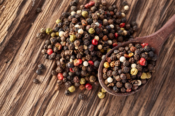 Top view on composition of peppercorn in wooden spoon on vintage wooden background, close-up, shallow depth of field