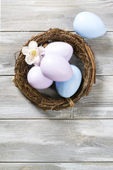 Colored easter eggs in a basket with spring flowers on a wooden gray background. Happy Easter