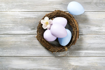 Colored easter eggs in a basket with spring flowers on a wooden gray background. Happy Easter. Flat lay