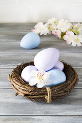 Hand-painted Easter eggs in a nest with spring flowers on a wooden gray background. Happy Easter