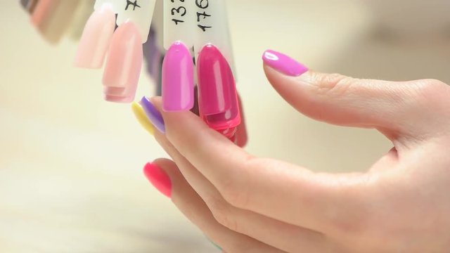 Slow motion nail color choice. Young woman hands with multicolored varnish on nails choosing nail color on nail colors palette in nail salon close up.