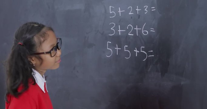 Confused female elementary school student solving a math problem on a blackboard in the classroom. Shot in 4k resolution