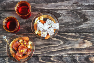 Turkish joys with different nuts is a glass of tea and a spoon. Eastern sweets. Traditional Turkish delight (Rahat lokum) on a wooden background. View from above .