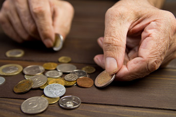 Hands of beggar with few coins. The concept of poverty . An elderly person on pension holds coins on wooden table background