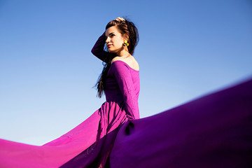 beautiful young woman in purple dress against the blue sky background