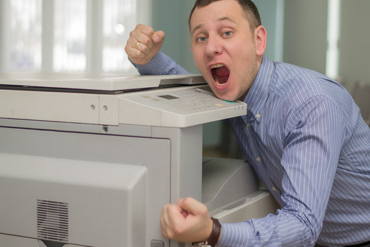 Angry Young Business Man Beats His Fist On A Multifunction Printer Or Copier