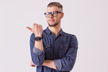 Studio shot of young male student in eyewear showing to copy space and smiling while standing...