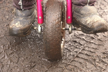 Child riding tricycle. The child rides a tricycle on a wet road