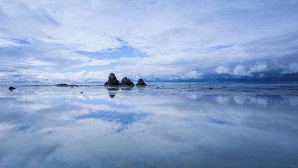 Reflection of the sky, rocks and clouds in calm sea water.