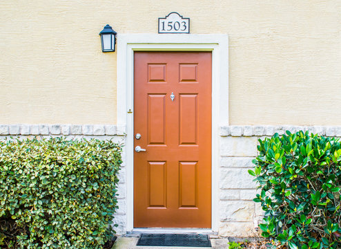 brown townhouse door in a tan limestone and stucco building with green hedges