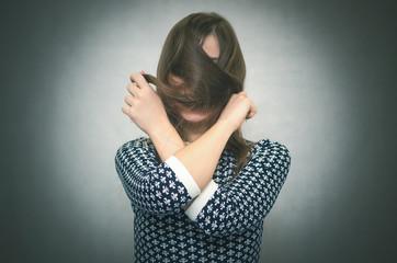 Fototapeta na wymiar Offended woman hides her face behind her hairs isolated on gray background. Incognito. Faceless person.