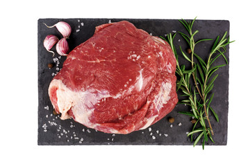 raw beef meat with rosemary and garlic on a black slate isolated on white background