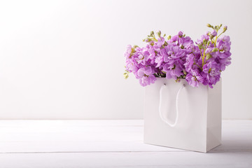 Lilac matthiola flowers in shopping bag over light gray stone background with copy space