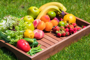 Various vegetables and fruits on a wooden tray against a background of green grass