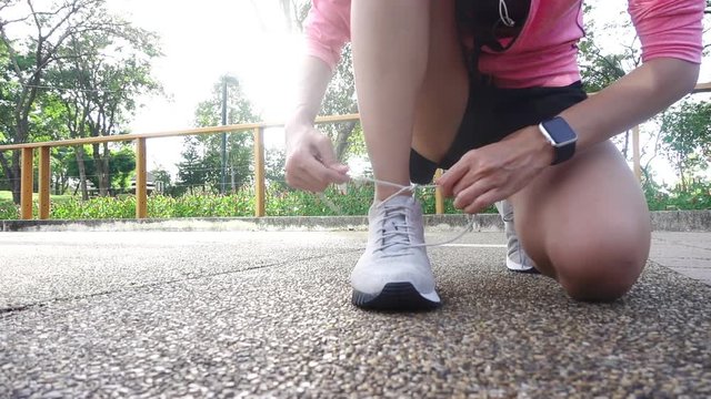 Slow motion - Close up of young woman lace up her shoe ready to workout on exercising in the park with warm light sunshine in morning. Young woman prepare for outdoor exercise in park.