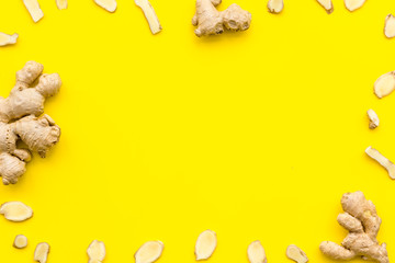 Whole and sliced ginger roots yellow background top view space for text