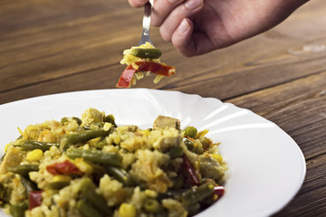 .Stewed vegetables, plate, hand and fork, wooden background