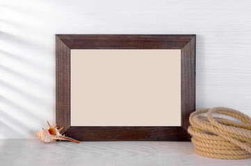 Obraz premium Blank wooden frame decorated with sea shell and rope on the white wooden table