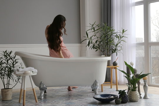 woman sitting near the  vintage retro bath in bathroom with big window