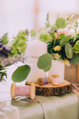 Beautiful composition on the table of wood slice, white candles, spools for thread and flower bouquets