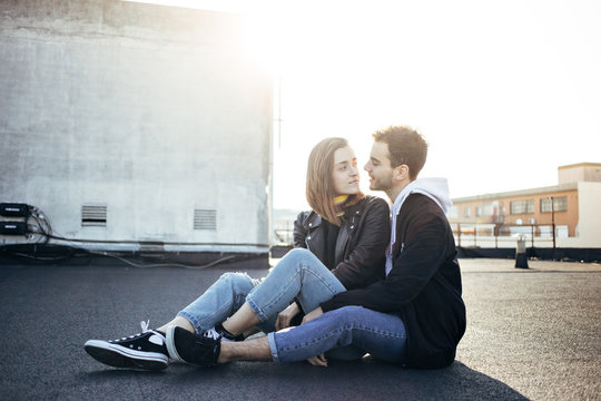 Stylish and trendy hip hipsters millennials couple, boyfriend and girlfriend sit on top of rooftop at sunset, look at each other fondly. Concept relationship goals of new generation, bloggers style