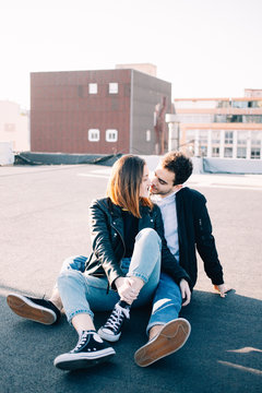 Stylish and trendy hip hipsters millennials couple, boyfriend and girlfriend sit on top of rooftop at sunset, look at each other fondly. Concept relationship goals of new generation, bloggers style
