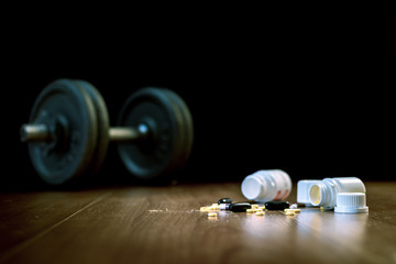 Steroid pills and capsules with dumbbell weight in the background - doping in sport.