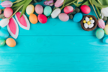 Easter composition with colored eggs, rabbit ears, nest and tulips on a blue wooden background.