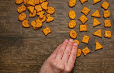 man's hand collects even row of crackers cookies on a wooden background. top view with copy space