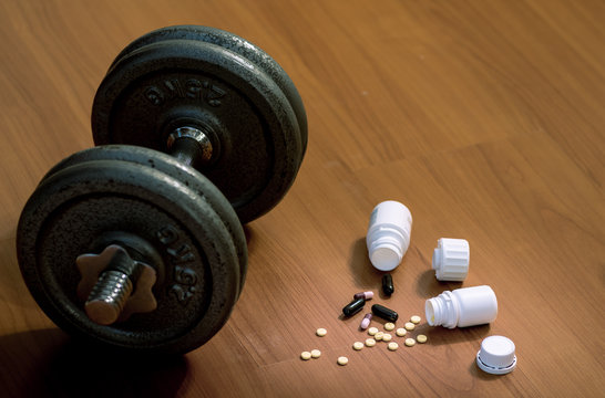 Steroid Pills And Capsules With Dumbbell Weight In The Background - Doping In Sport.