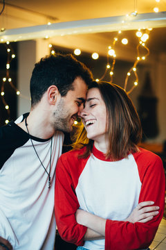 Happy and adorable, couple of cute young teenagers or millennials, laugh smile and cuddle inside apartment or studio with holiday lights, wear baseball shirts, excited about love and relationship