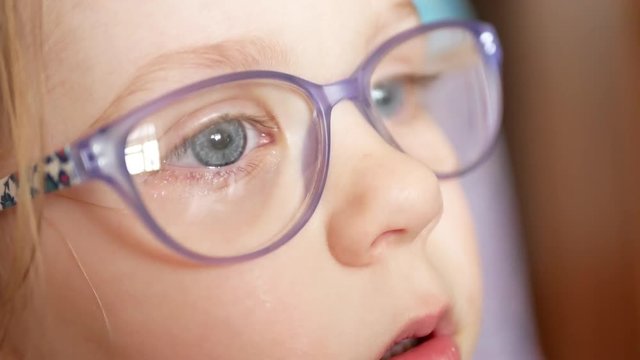 A little blue-eyed girl with blond hair in glasses looks at something