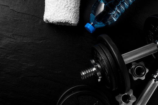 Dumbbell, bottle of water and white towel on black background. Gym accesories.