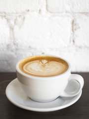 Cup of cappuccino on wooden table with white brick wall background.