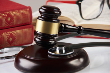 Law books with wooden judges gavel and medical stethoscope on white table in a courtroom or enforcement office, close-up. Medicine law concept.