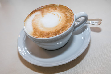 Cappuccino mit Milchschaum in Tasse auf Tischdecke