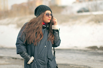 young attractive woman fashionista with red lipstick walking in a black down jacket and glasses in the winter on the street