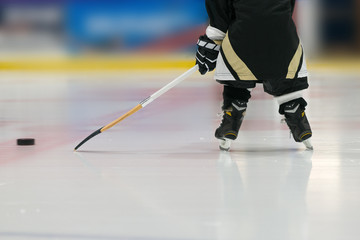 Toddler is playing hockey with stick and puck. Photo has been taken from back: skates and stick are shown. 