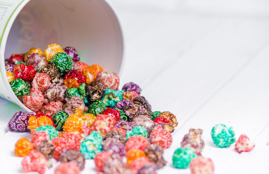 Brightly Colored Candied Popcorn, white background. Horizontal image of Junk food, fruit flavored popcorn in light pink bowl. Colorful, rainbow, candy coated popcorn. Shallow focus on popcorn in bowl.
