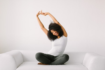 An African American young women sitting in the lotus position on white bed