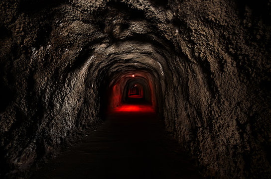 Fototapeta Infinite tunnel with an ominous red backlight through the rock